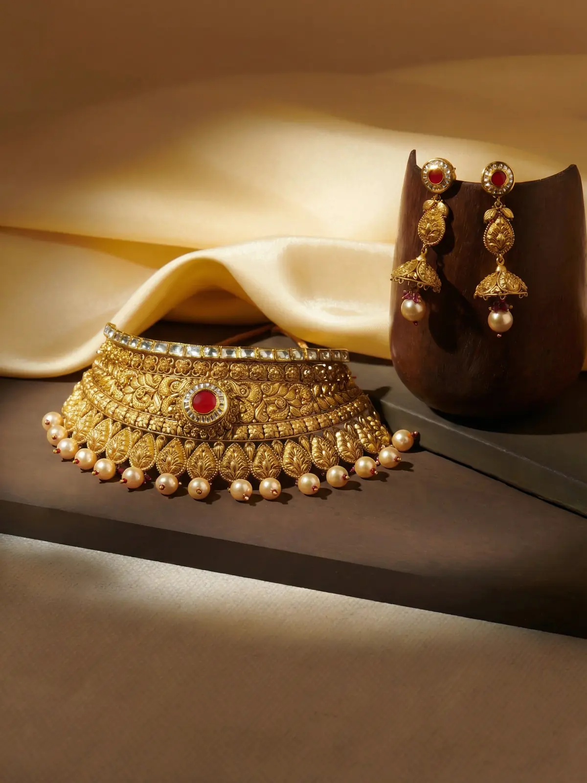 Close-up: ornate gold jhumka earrings on rich silk with zari embroidery.